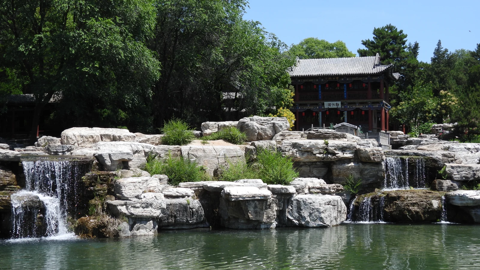 A garden waterfall flowing over rocks surrounded by greenery.