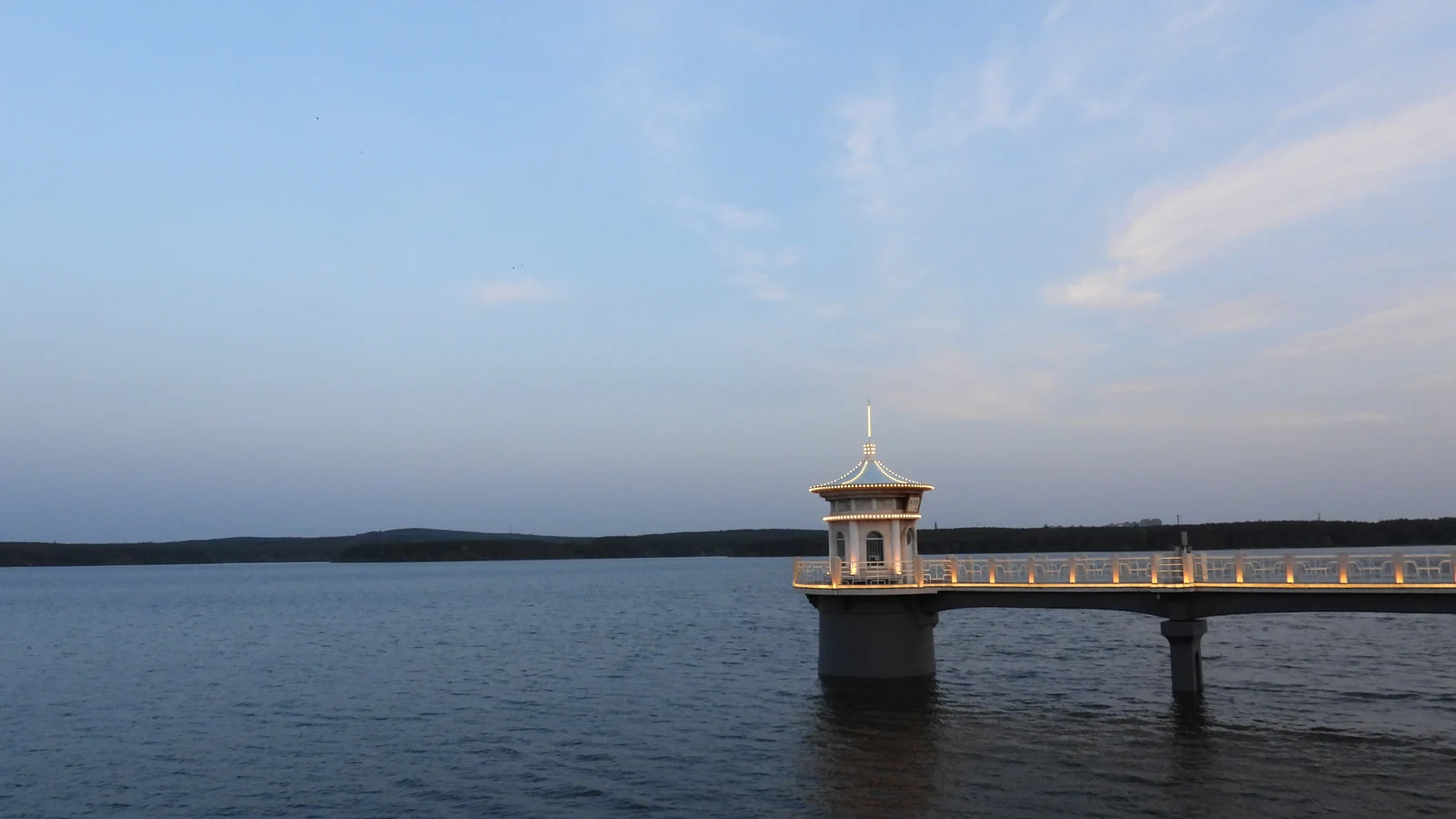 A lake and illuminated pavilion beneath a blue evening sky.